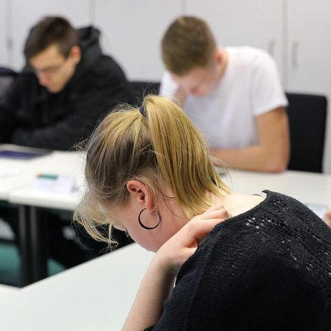 Zwei junge Frauen und zwei junge Männer sitzen über ihrer Theorieprüfung für den Führerschein gebeugt