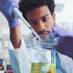 Ein junger Mann mit dunklen Locken tröpfelt in einem Labor etwas mit einer Pipette in eine Petrischale