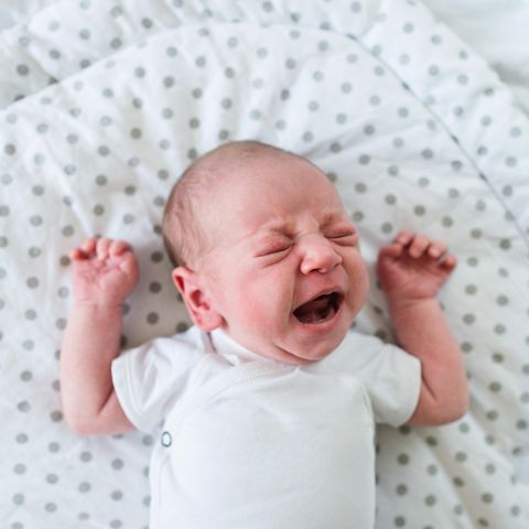 Ein Baby liegt im Bett und schreit
