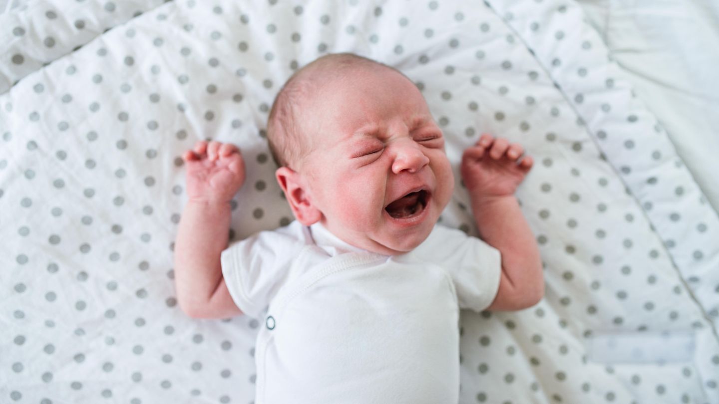 Ein Baby liegt im Bett und schreit
