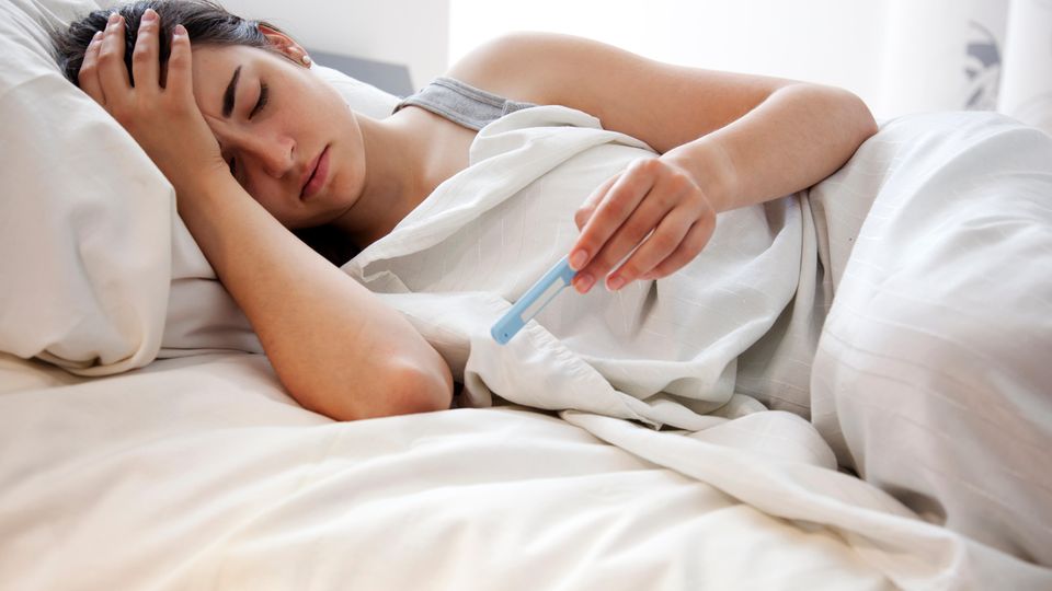 Eine Frau liegt mit Schüttelfrost und Fieber im Bett