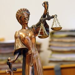 Eine kleine goldene Statue der Justizia steht vor einem Haufen Akten