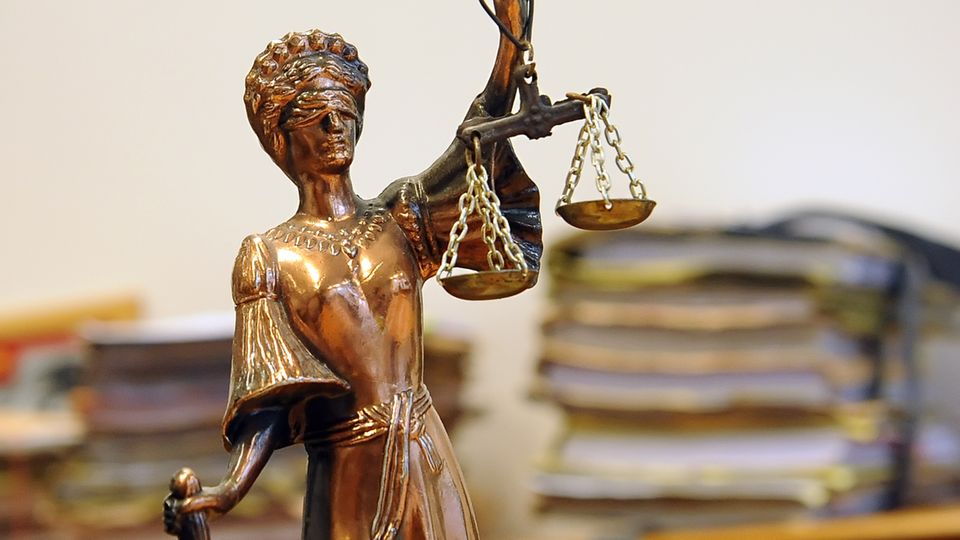Eine kleine goldene Statue der Justizia steht vor einem Haufen Akten