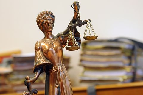 Eine kleine goldene Statue der Justizia steht vor einem Haufen Akten