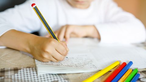 Ein Kind schreibt mit einem Bleistift in ein Schreibheft