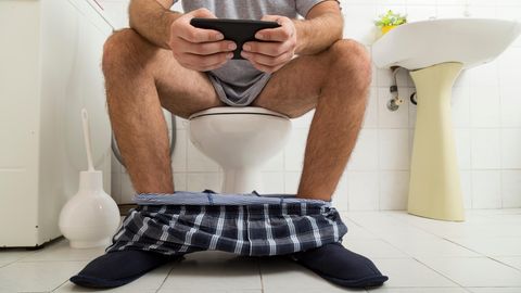 Eine Mann sitzt auf der Toilette und tippt ins Smartphone