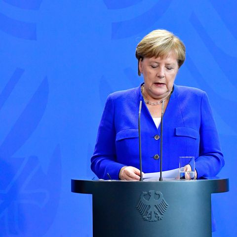 Recep Tayyip Erdogan steht links und schaut auf das Rednerpult vor sich, während Angela Merkel rechts am Pult steht und spricht