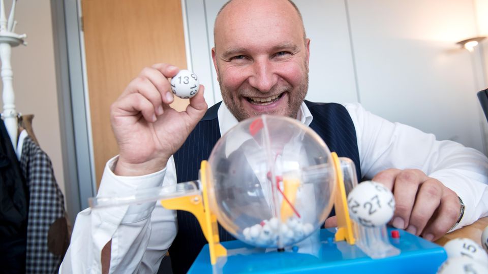 Rainer Holmer, Gewinnbetreuer von Lotto Bayern, sitzt in seinem Büro an einem Spielzeug-Ziehungsgerät für Lottokugeln
