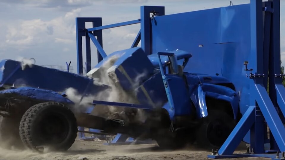 Ein blauer LKW zerschellt in einem Crashtest an einer massiven Stahlwand