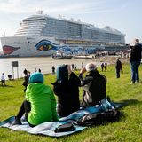 Viele Sehleute auf dem Deich: Sie beobachten, wie das Kreuzfahrtschiff "Aida Nova" während der Überführung auf der Ems von Schleppern durch das Ems-Sperrwerk Gandersum manövriert wird.