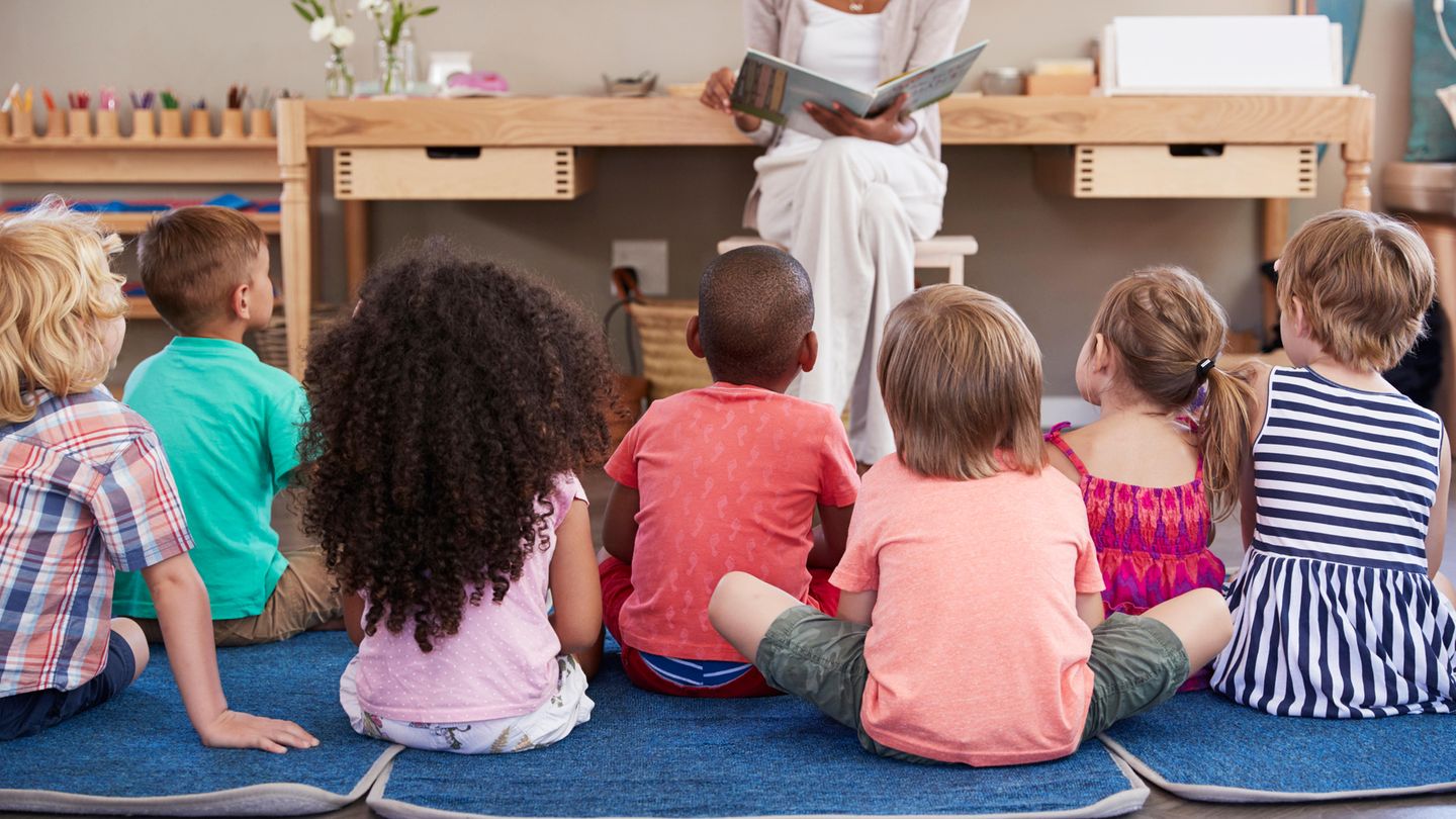 Erzieherin liest Geschichte aus Buch, Kinder sitzen vor ihr