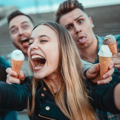 Junge Erwachsene halten Eistüten in den Händen und scherzen für ein Selfie