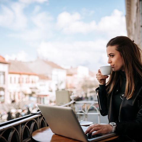 Frau sitzt auf einem Balkon an einem Laptop