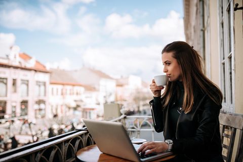 Frau sitzt auf einem Balkon an einem Laptop