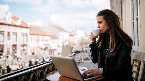 Frau sitzt auf einem Balkon an einem Laptop