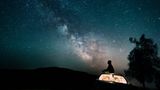 Mann sitzt und guckt in Sternenhimmel