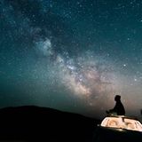 Mann sitzt und guckt in Sternenhimmel