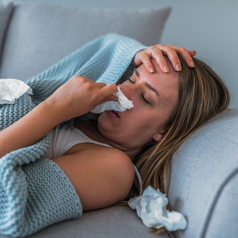 Eine Frau liegt mit Fieber und Erkältung auf dem Sofa (Bebilderung Superinfektion mit Bakterien)