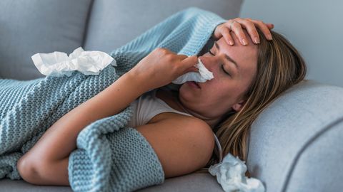 Eine Frau liegt mit Fieber und Erkältung auf dem Sofa
