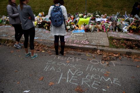 Drei junge Frauen stehen vor einem Meer aus Blumen und Kerzen und trauern um die Opfer von Pittsburgh