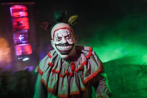 Ein Mann mit einer böse grinsenden Clownsmaske steht vor grün beleuchtetem Nebel