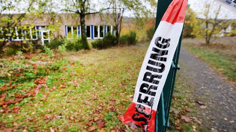 An einem grünen Drahtzaun hängt ein Ende eines rot-weißen Flatterbandes mit "Polizeiabsperrung" darauf