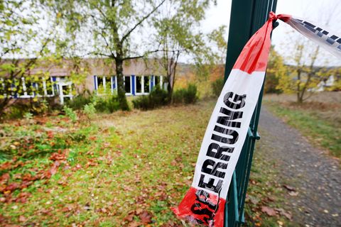 An einem grünen Drahtzaun hängt ein Ende eines rot-weißen Flatterbandes mit "Polizeiabsperrung" darauf