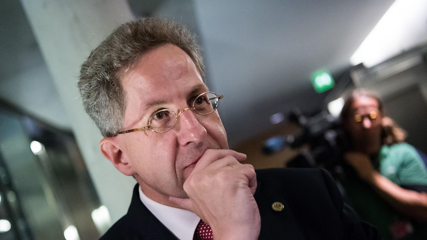 Hans-Georg Maaßen, ein Mann mit grauen Haaren und kleiner, goldener Nickelbrille, hält sich die rechte Hand vor den Mund
