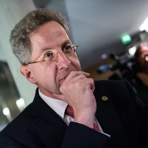 Hans-Georg Maaßen, ein Mann mit grauen Haaren und kleiner, goldener Nickelbrille, hält sich die rechte Hand vor den Mund