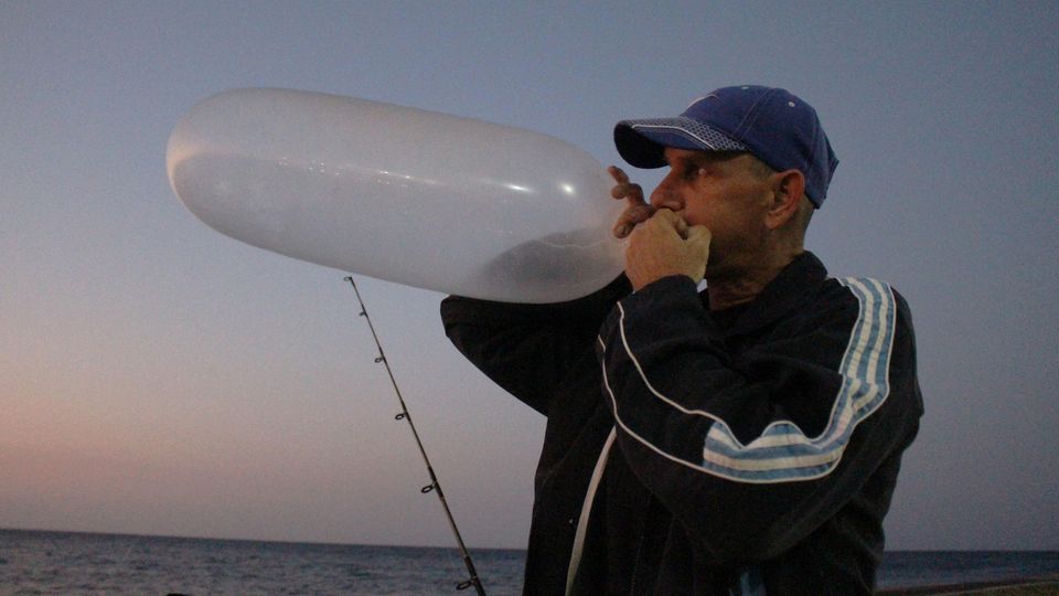 Kuba, Havanna: Ein Angler bläst ein Kondom auf, um es als Schwimmer zu nutzen.