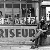 Ein langhaariger junger Mann vor einem Friseur-Schaufenster mit adretten Kurzhaarfrisuren