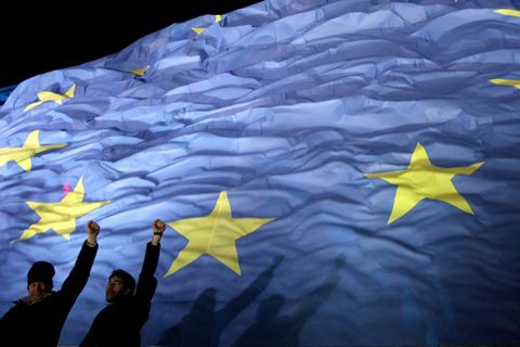 Zwei Personen recken vor einer EU-Flagge ihre Faust in die Höhe