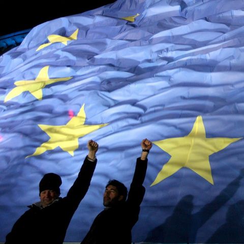 Zwei Personen recken vor einer EU-Flagge ihre Faust in die Höhe