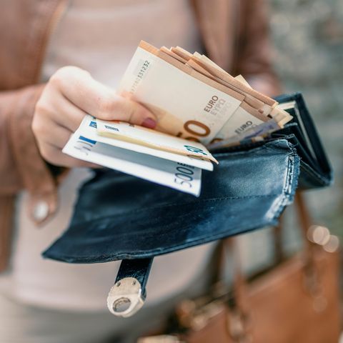 Eine Frau in hellbrauner Lederjacke zieht etliche Euroscheine aus ihrem großen Portemonnaie