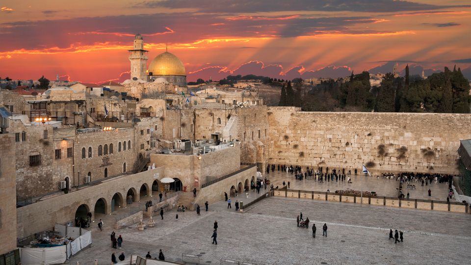 In Jerusalem geht über Felsendom und Klagemauer die Sonne unter. Der Himmel ist orangerot gefärbt