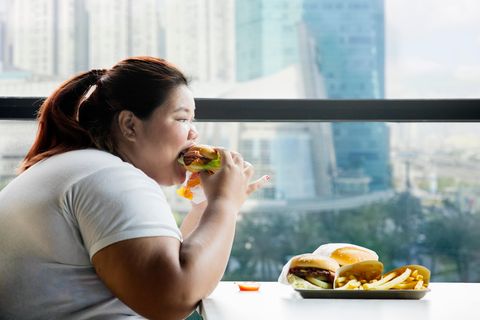 Eine übergewichtige Frau isst Burger und Pommes