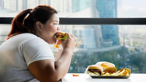 Eine übergewichtige Frau isst Burger und Pommes