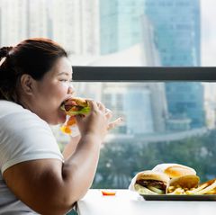 Eine übergewichtige Frau isst Burger und Pommes
