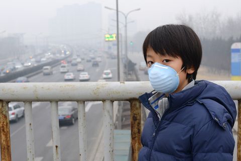 Ein junge steht auf einer Brücke im Smog. Er trägt eine Atemschutzmaske