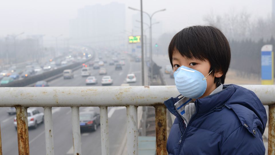 Ein junge steht auf einer Brücke im Smog. Er trägt eine Atemschutzmaske