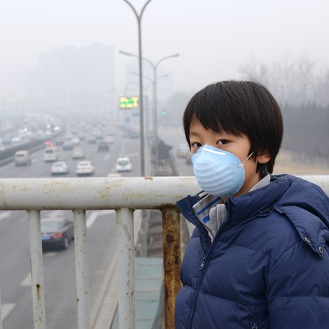 Ein junge steht auf einer Brücke im Smog. Er trägt eine Atemschutzmaske