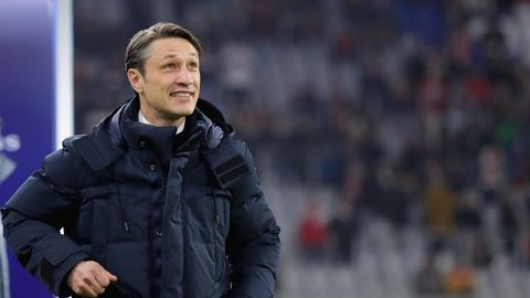 In dunkelblauer Winterjacke steht Niko Kovac am Spielfeldrand und grinst beim Blick auf den Spielstand