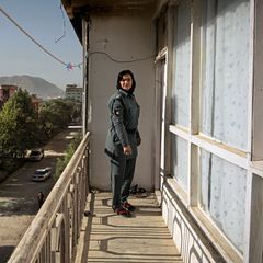 Schamila steht in Uniform auf dem Balkon ihrer Wohnung. Im Hintergrund kann man die Berge des Hindukuschs erkennen. Schamila wurde als Zwölfjährige entführt und von Afghanistan nach Pakistan verschleppt.