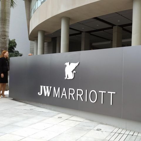 Auf einer silbergrauen Metallwand ist der weiße Schriftzug "JW Marriott" zu sehen. Daneben stehen zwei Männer in Anzügen