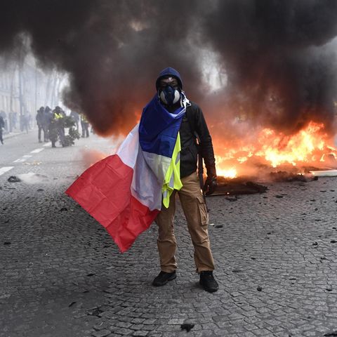 Paris, achtes Arrondissement: Ein "Gelbwesten"-Demonstrant posiert mit einer französischen Fahne vor einem brennenden Auto für die Kamera. Die Wut der Protestbewegung richtet sich aber auch gegen Präsident Macron und dessen Reformpolitik.