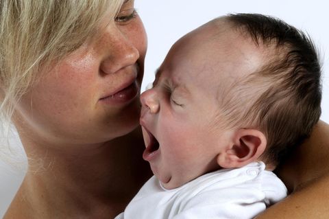 Eine müde Mutter hält ihr schreiendes Baby im Arm