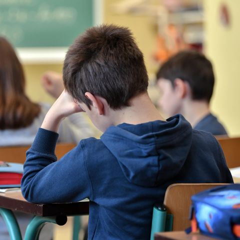Schüler sitzt mit abgestützter Hand in Schulklasse