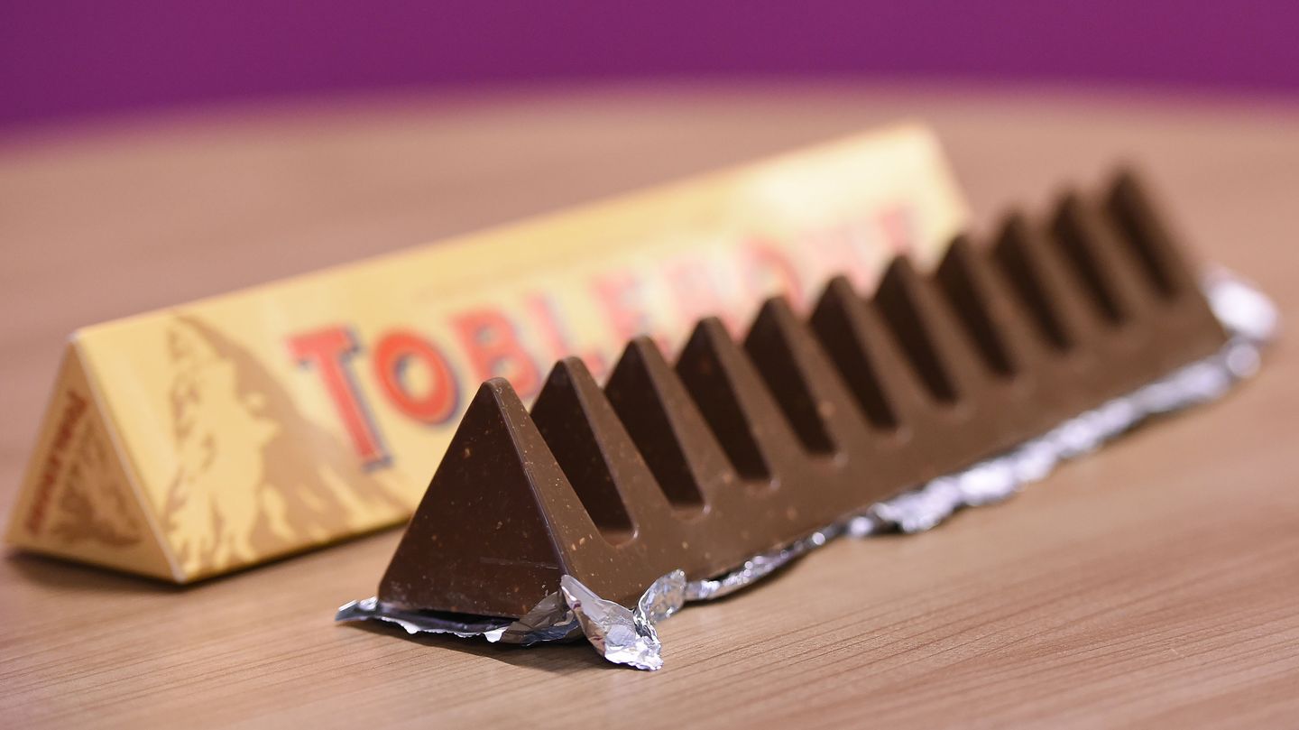 Ein dreieckiger Tobleroneriegel liegt ausgepackt neben der Verpackung