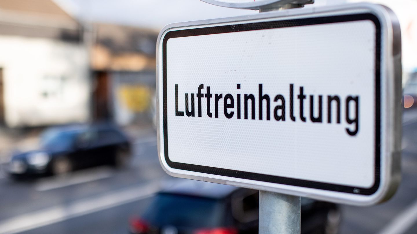 An einer mehrspurigen Straße steht ein Schild "Luftreinhaltung", im Hintergrund fahren Autos