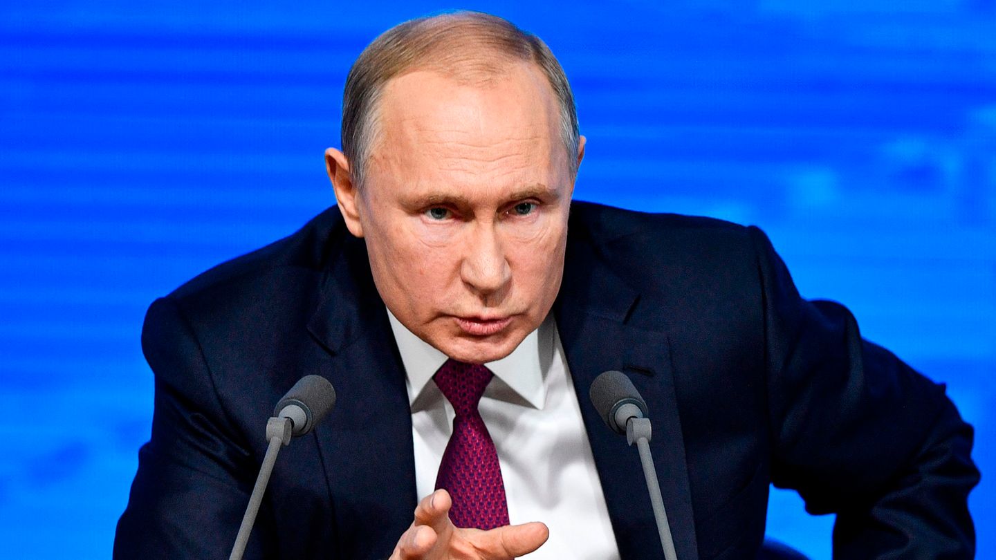 Russlands Präsident Wladimir Putin sitzt hinter zwei Mikros und vor einer blauen Wand während einer Pressekonferenz